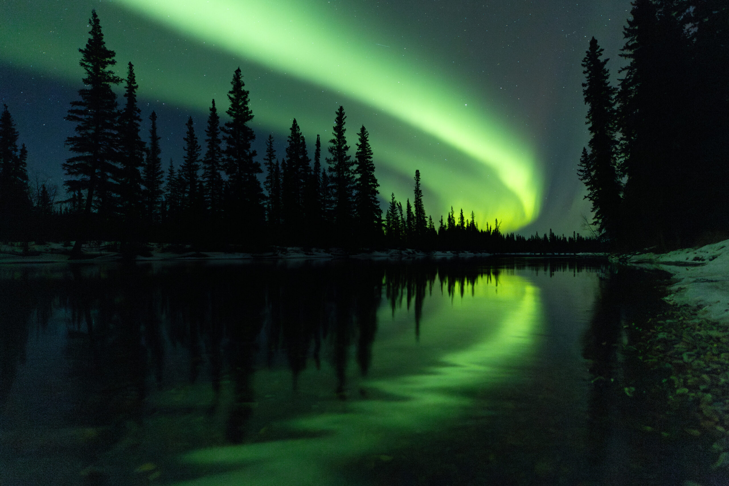 A wide arc of bright green aurora borealis lights reflecting perfectly in a calm body of water.
