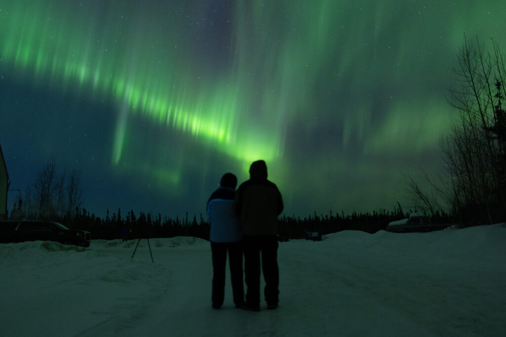 2 people standing watching the aurora borealis near Fairbanks, Alaska.